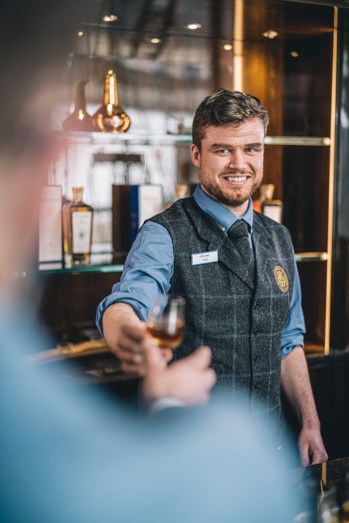 Smartly dressed barman presenting a glass of whisky.