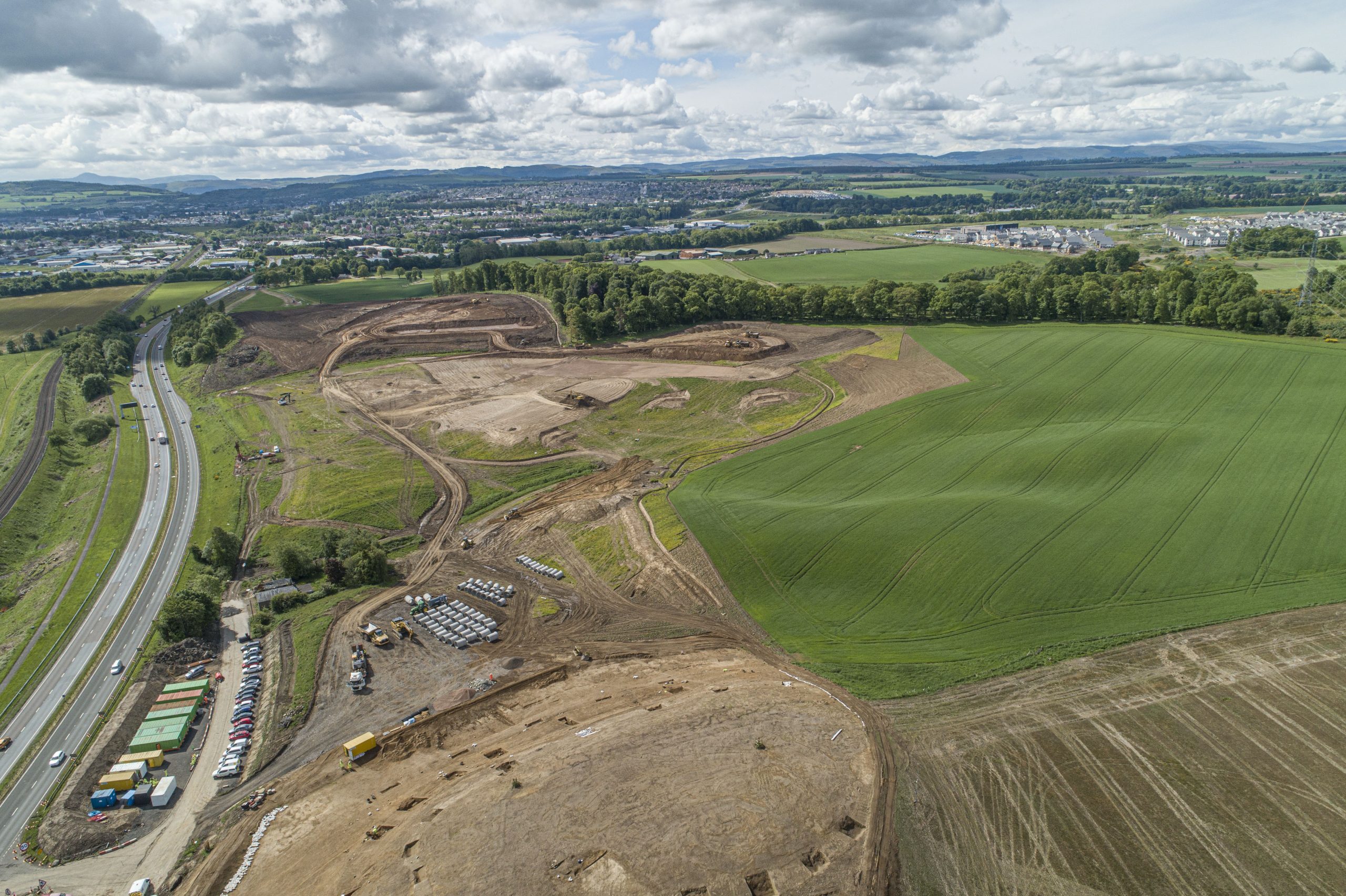 drone image of construction site containing a car park, shipping containers and muddy roads.